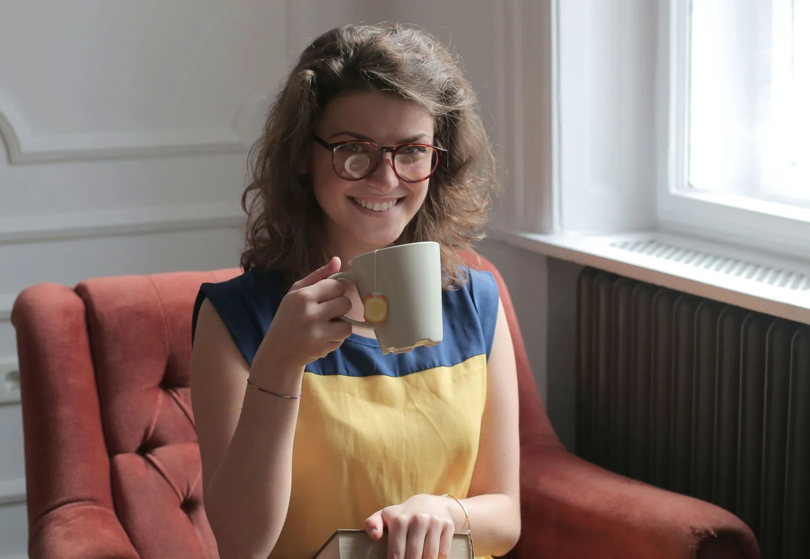 A woman relaxing with a cup of tea by a window at home
